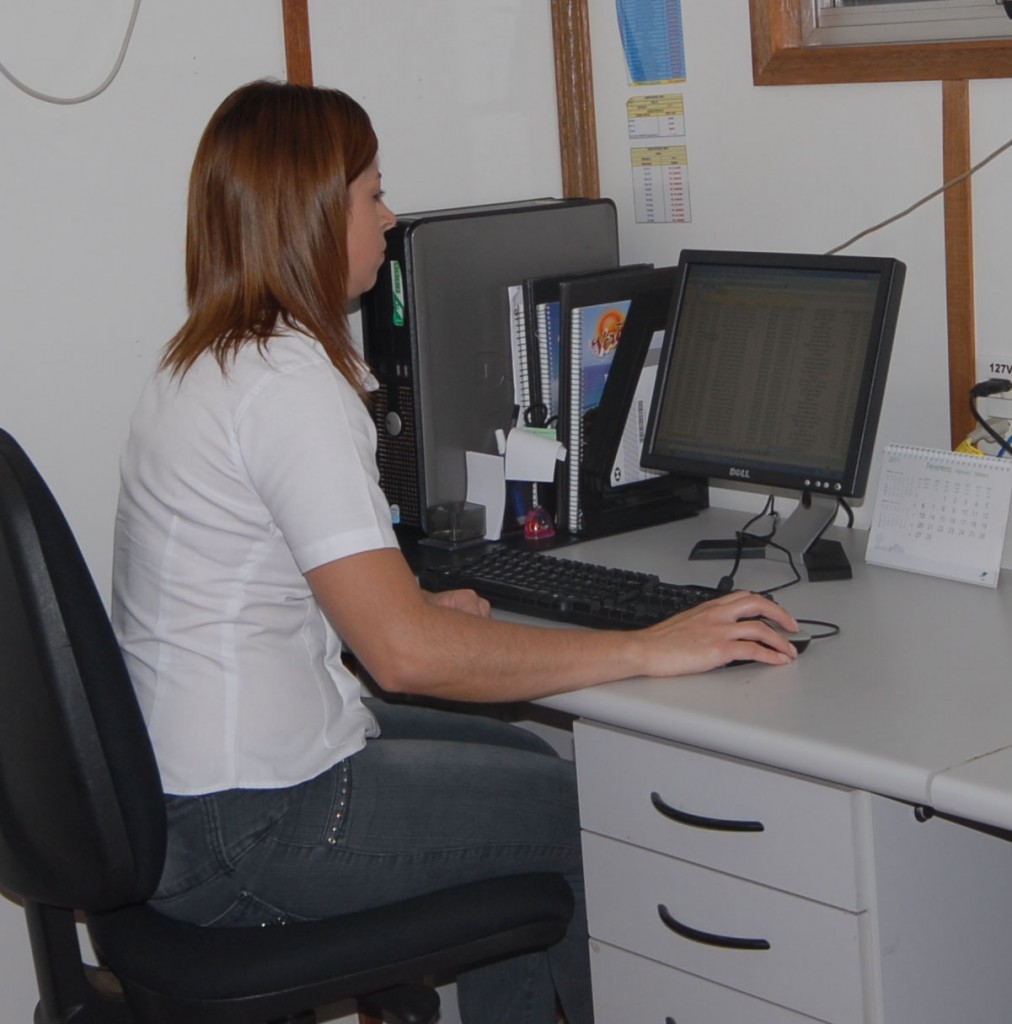 Una mujer en ropa de oficina sentada en un escritorio trabaja en la computadora. 