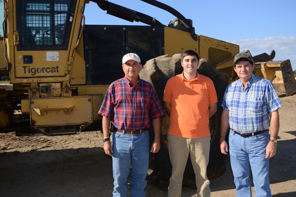 B&G Equipment sales specialist Cleve Altman, general manager Manuel Henderson and Glenn Henderson. stand together in front of a Tigercat skidder.