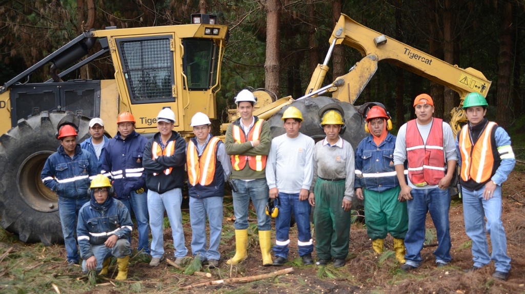 El equipo de cosecha de COTOPAXI S. A; un grupo numeroso de hombres posan juntos delante de un skidder 620D de Tigercat.