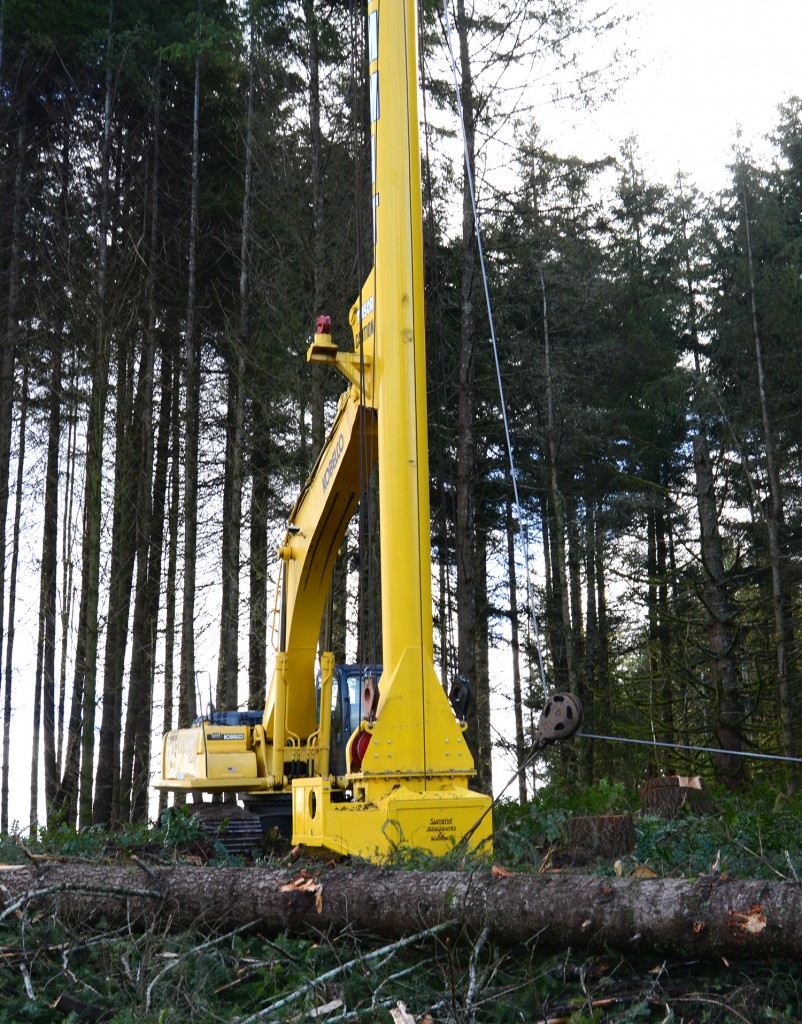 An unmanned excavator equipped with a winch and yarder tower sits at the top of the hill.