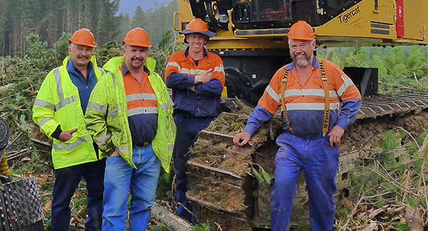 (Da esquerda para a direita) Robert, Kevin, Nicholas (Tiny) e Geoffrey Muskett em um local de trabalho em frente a uma máquina de esteira Tigercat.