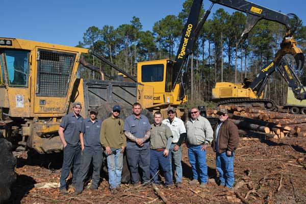 One of the three Dopson crews. (L-R) Billy Robertson (skidder operator), Henry Brown aka Pine Cone (loader operator), Pedro Zarraga (truck driver), Charlie Dopson, Timmy Dopson, Glynn Lambert (loader operator), Jimmy Watkins (Tidewater sales specialist), Don Snively (Tigercat district manager).