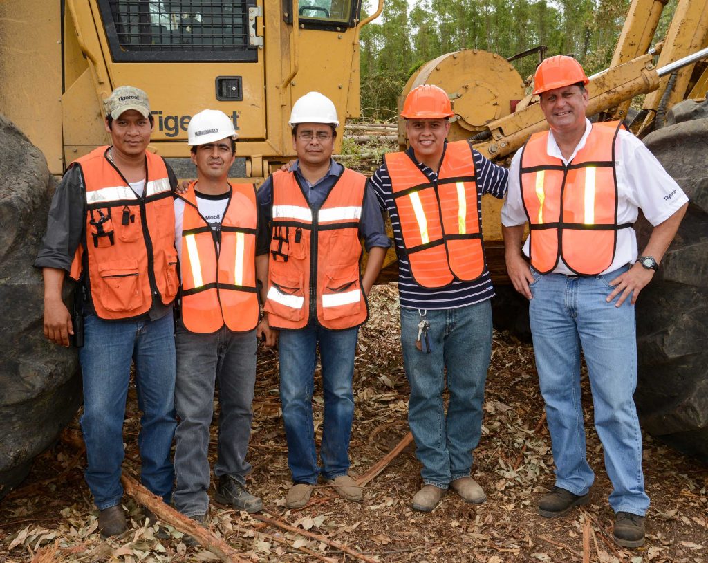 5 men stand together in front of a Tigercat skidder wearing safety vests and hats.