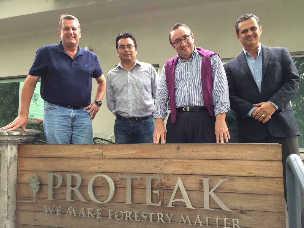 4 hommes se tiennent fiers et souriants devant un panneau de Wood Proteak où l'on peut lire « we make forestry matter » (avec nous, l’exploitation forestière compte)