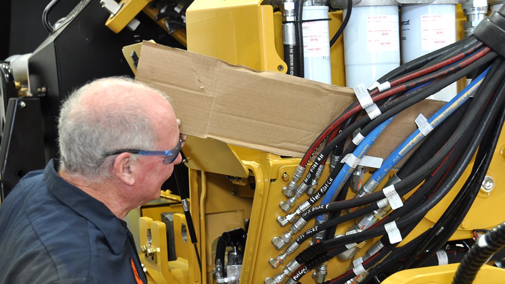 Un technicien vérifiant la présence de fuites hydrauliques à l'aide d'une feuille de carton.