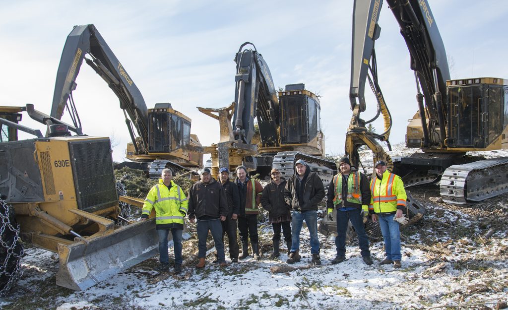 8 men stand infront of 4 Tigercat machines.