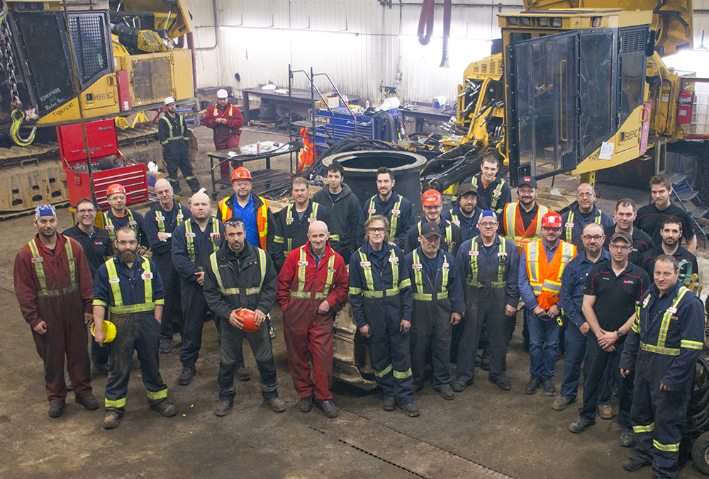 A large group of people in a warehouse wearing safety coveralls. Some coveralls are red, others are navy blue.