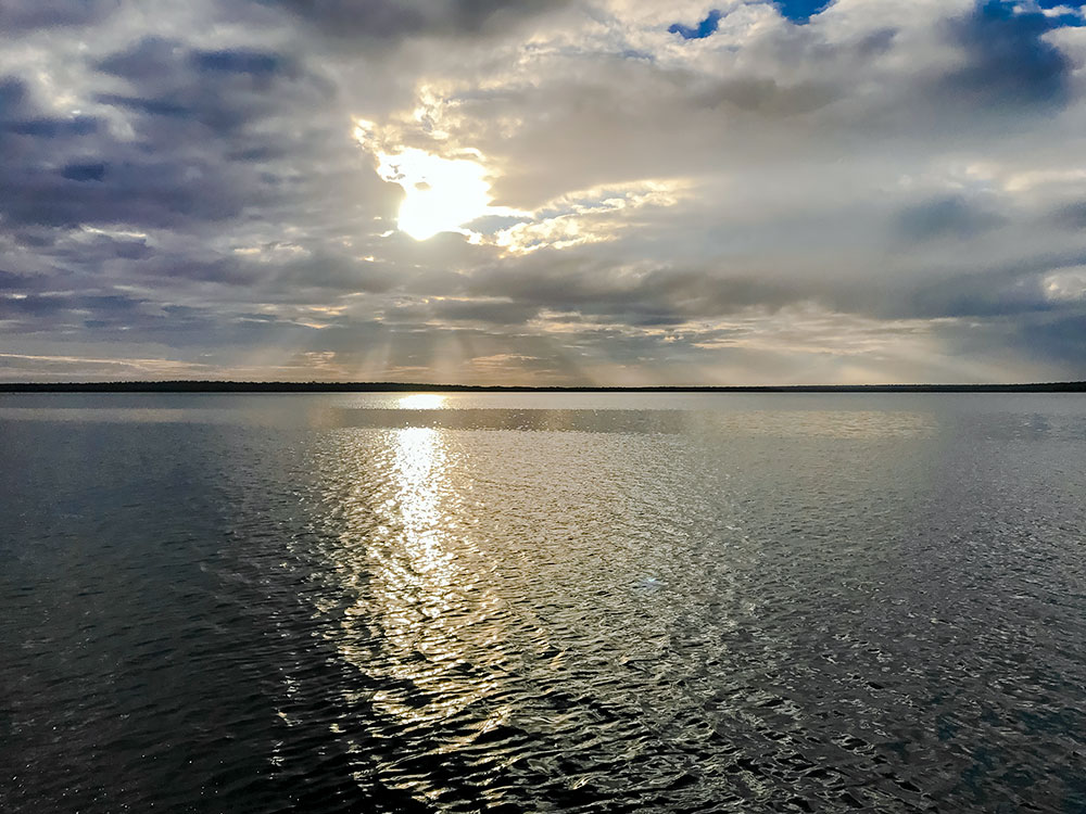 Un paisaje lacustre; los rayos del sol atraviesan las nubes y se extienden desde el cielo hasta el agua. 