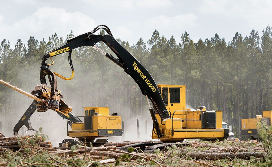 Процессор H250D компании Sanders Logging на фоне двух погрузчиков Tigercat.