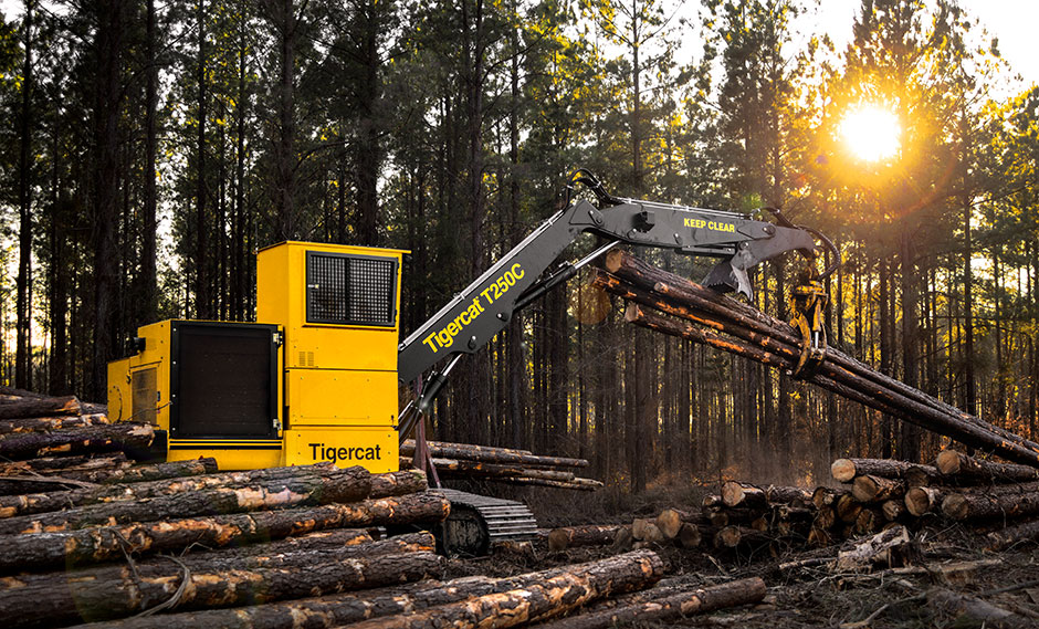 A Tigercat T250C Loader on a jobsite, a pile of logs in the foreground leads to the heavy logging machine.