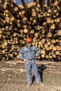 Portrait de Bernard Fortin, directeur général de Peace River Logging, posant devant une pile de billes.