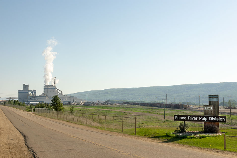 An exterior view of the entrance to Peace RIver Logging's chipping yard. A sign out front reads, "Peace River Pulp Division"