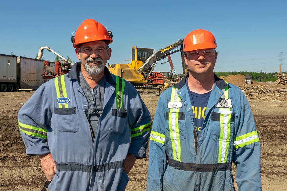 Bernard Fortin and Erik Lokseth stand infront of a Tigercat 875 logger on site at Peace River Pulp Division.