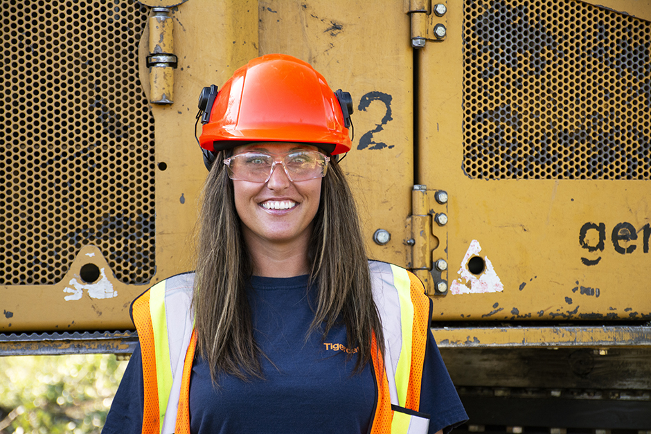 Lisa Schneider stands in front of a Tigercat machine.