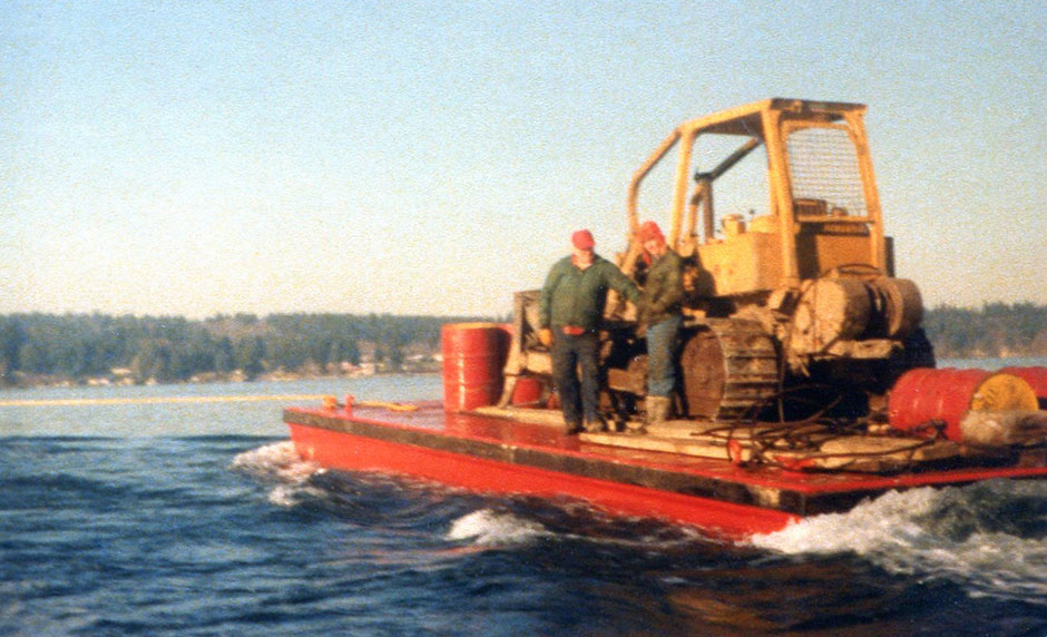 Le père et le grand-père d'Adam avec leur bulldozer HD-6 se dirigeant vers l'île de Squaxin sur une barge.